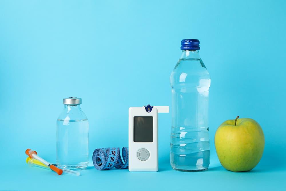 Insulin, measuring tap, blood sugar monitor, water, and apple