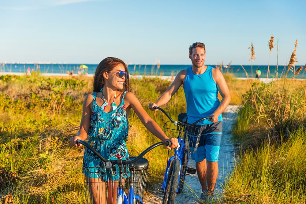 A man and a woman walking from a beach with their bikes