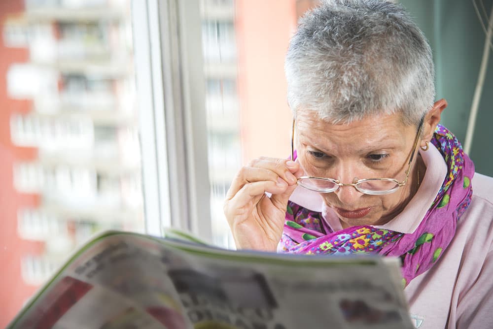 Senior woman with glasses struggling to read a newspaper
