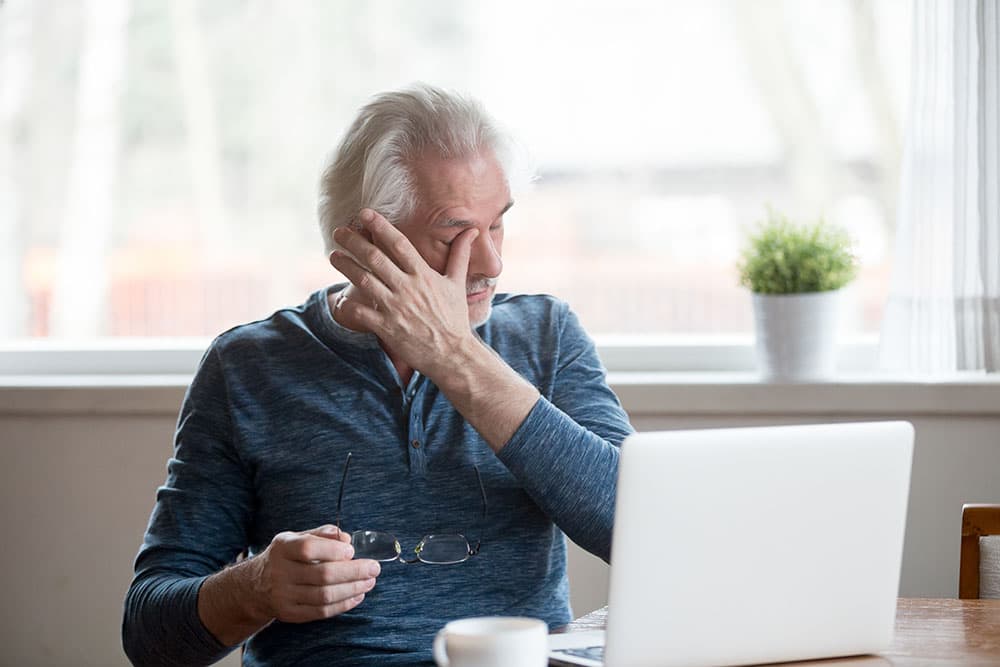 An older man using a laptop and suffering from dry eyes
