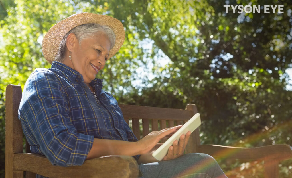 a person smiling sitting on a bench and reading about the symptoms and causes of cataracts